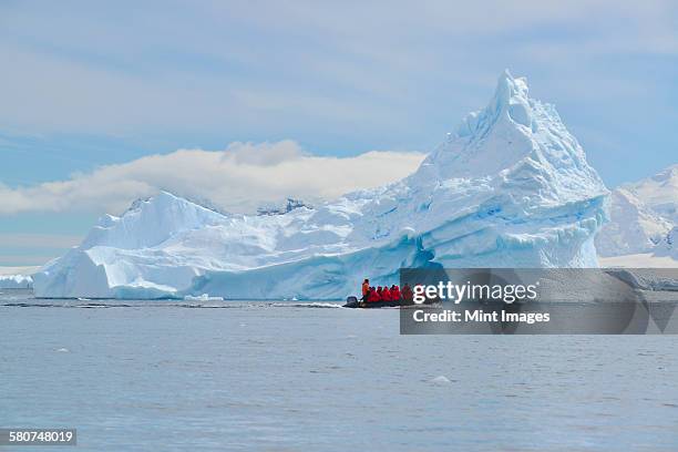 group of people in a rubber boat near a towering iceberg in the antarctic. - antarctica people stock pictures, royalty-free photos & images
