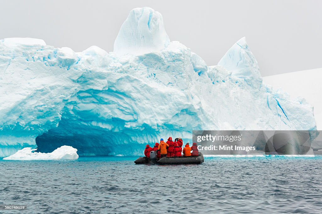 Group of people crossing the ocean in the Antarctic in a rubber boat, icebergs in the background.