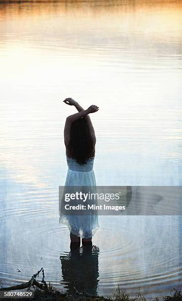 a woman in a white dress in shallow water at dusk - see through negligee stock-fotos und bilder