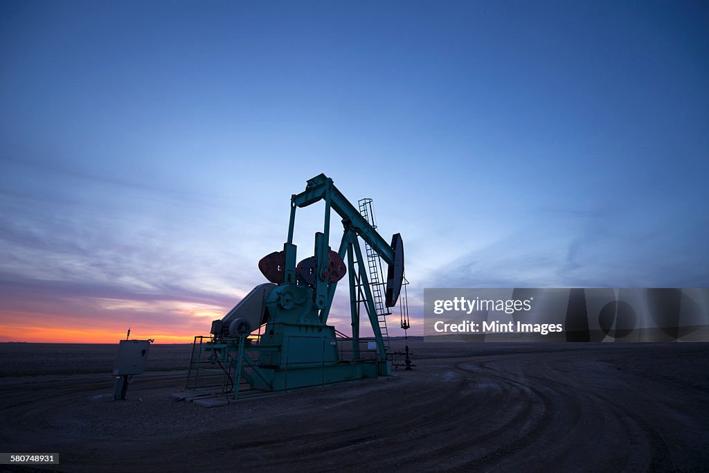 A pumpjack at an oil drilling site at sunset.