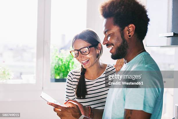 happy young couple with phablet in their kitchen - happy couple using cellphone stockfoto's en -beelden