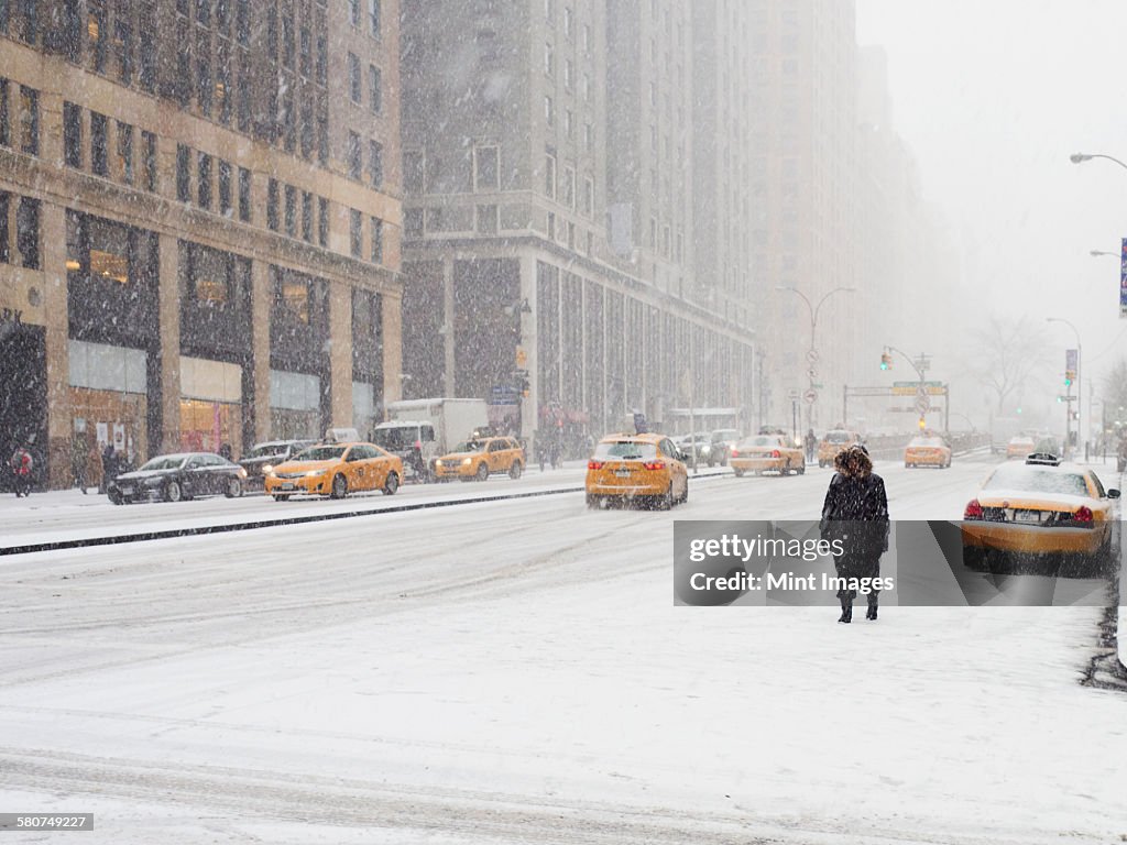 Man walking in a city in the snow during a blizzard, yellow taxis on the street.