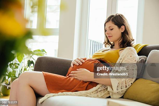 pregnant woman holding her baby belly while relaxing on couch at home - gravid mage bildbanksfoton och bilder