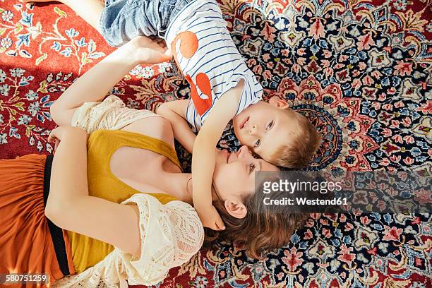 mother and little son cuddling on a persian rug at home - two kids looking at each other stockfoto's en -beelden