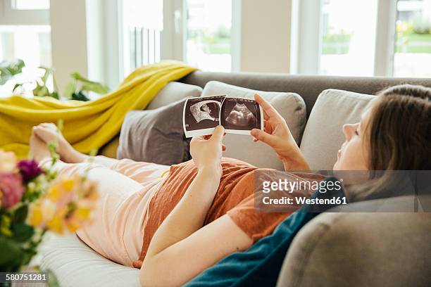 pregnant woman looking at ultrasound scan while relaxing on the couch - embarazada fotos fotografías e imágenes de stock