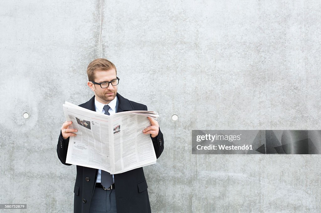 Businessman reading newspaper at concrete wall