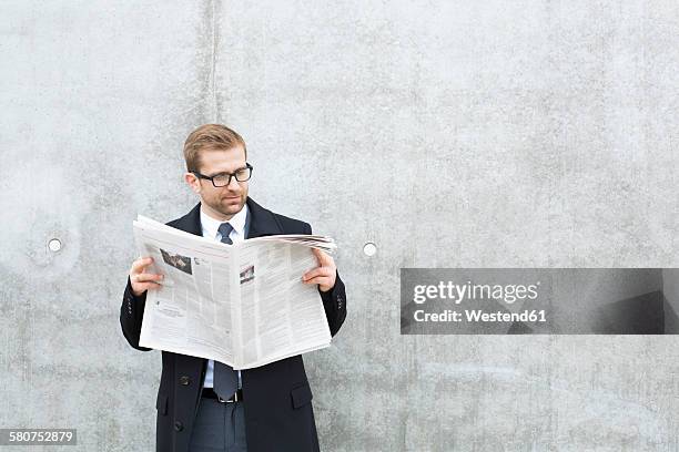 businessman reading newspaper at concrete wall - newspaper stockfoto's en -beelden