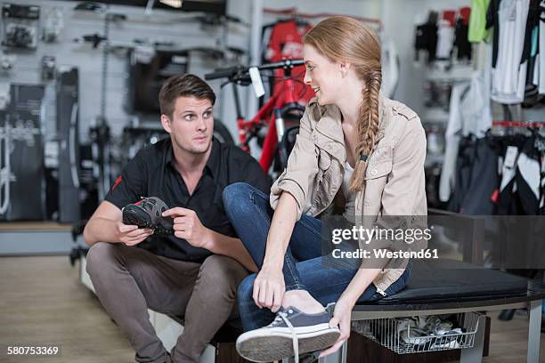 young woman buying bicycle shoes, salesman advising - sporthandel stock-fotos und bilder