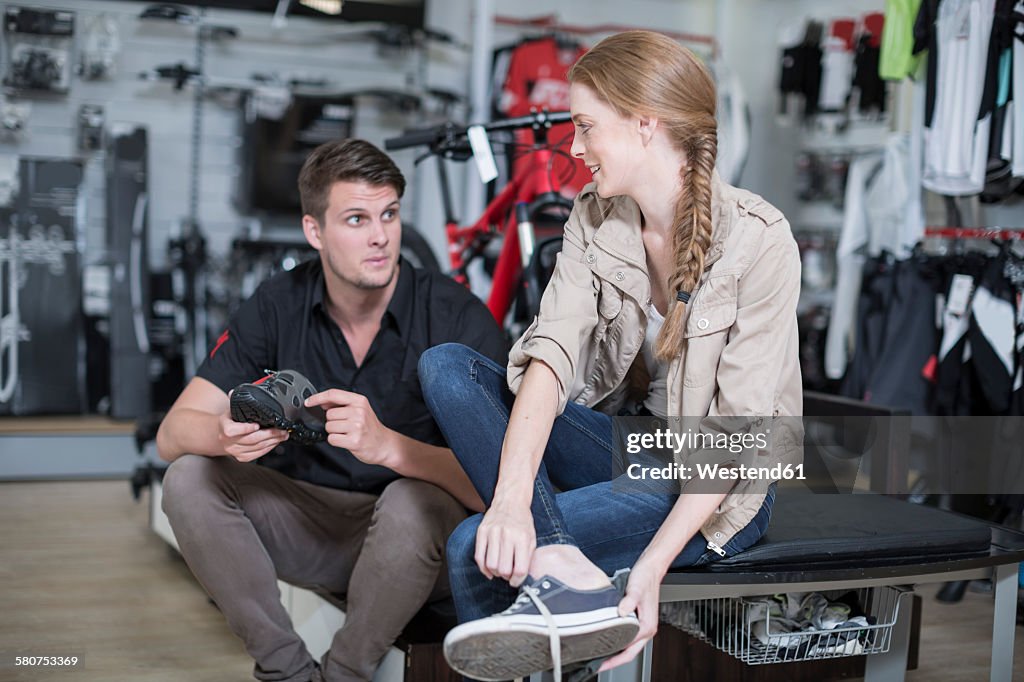 Young woman buying bicycle shoes, salesman advising