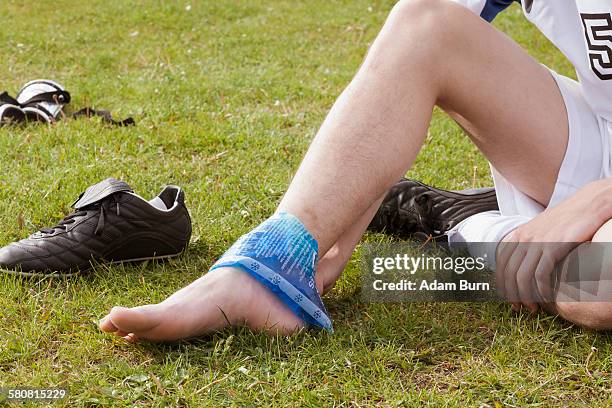 low section of soccer player applying ice pack on ankle in field - ankle sprain stock-fotos und bilder