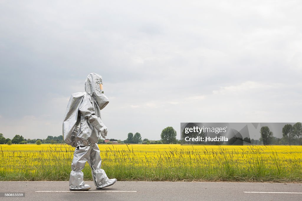 A person in a radiation protective suit walking alongside an oilseed rape field