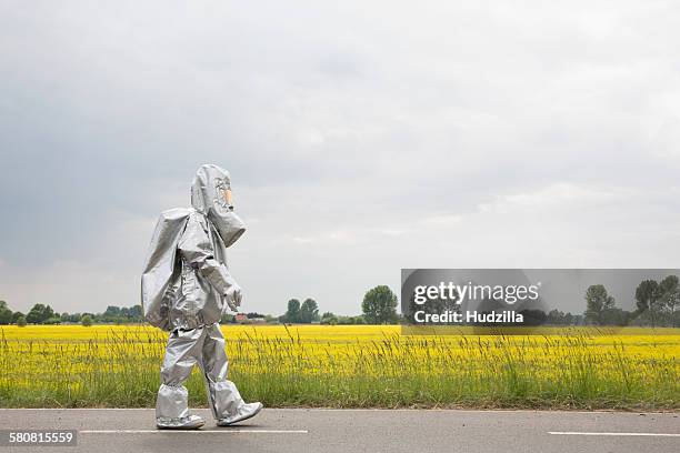 a person in a radiation protective suit walking alongside an oilseed rape field - roupa protetora imagens e fotografias de stock