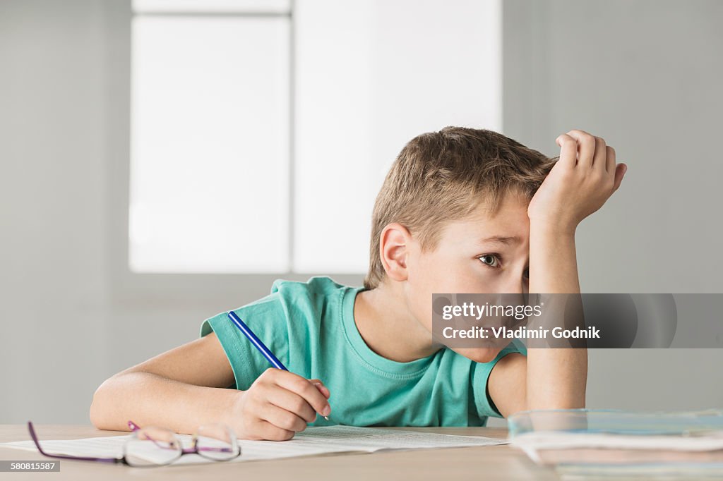 Bored boy with hand on forehead doing homework at home