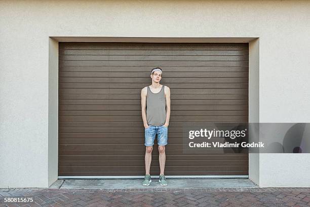 full length portrait of young man standing against garage door - calções imagens e fotografias de stock