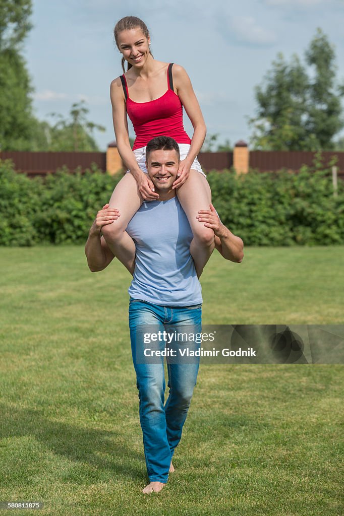 Full length portrait of happy young man carrying woman on shoulders in backyard
