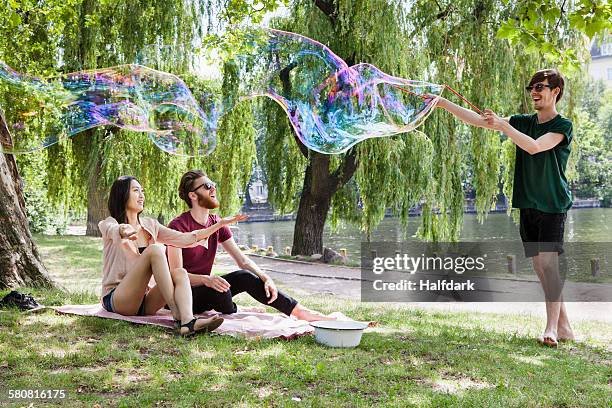 happy friends enjoying with large bubble at park - bubbles happy stockfoto's en -beelden