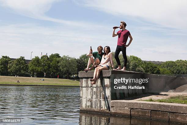 multi-ethnic friends enjoying on retaining wall by canal - 3 men standing outdoors stock pictures, royalty-free photos & images