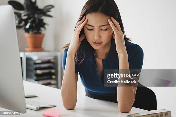 young businesswoman suffering from headache at desk in office - asian woman angry stock pictures, royalty-free photos & images