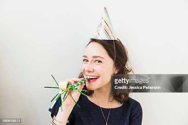 smiling young woman with party horn blower - partyhut stock-fotos und bilder
