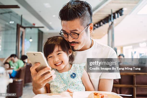 young dad using smartphone with little daughter - family technology stockfoto's en -beelden