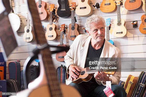 man playing ukulele in shop - ukulele stock-fotos und bilder