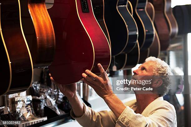 man picking out guitar in shop - loja de música imagens e fotografias de stock