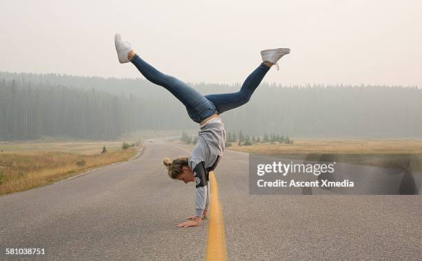 young woman performs handstand on rural road - fare la verticale sulle mani foto e immagini stock