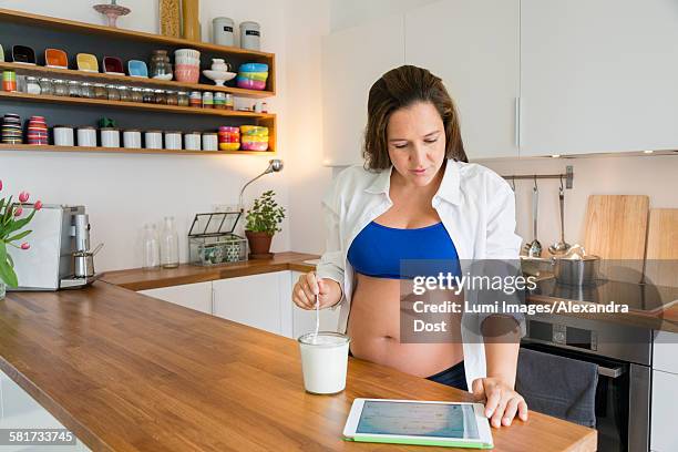 pregnant woman eats yogurt while using tablet - alexandra dost stockfoto's en -beelden