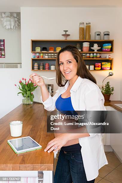 pregnant woman eats yogurt while using tablet - alexandra dost stockfoto's en -beelden