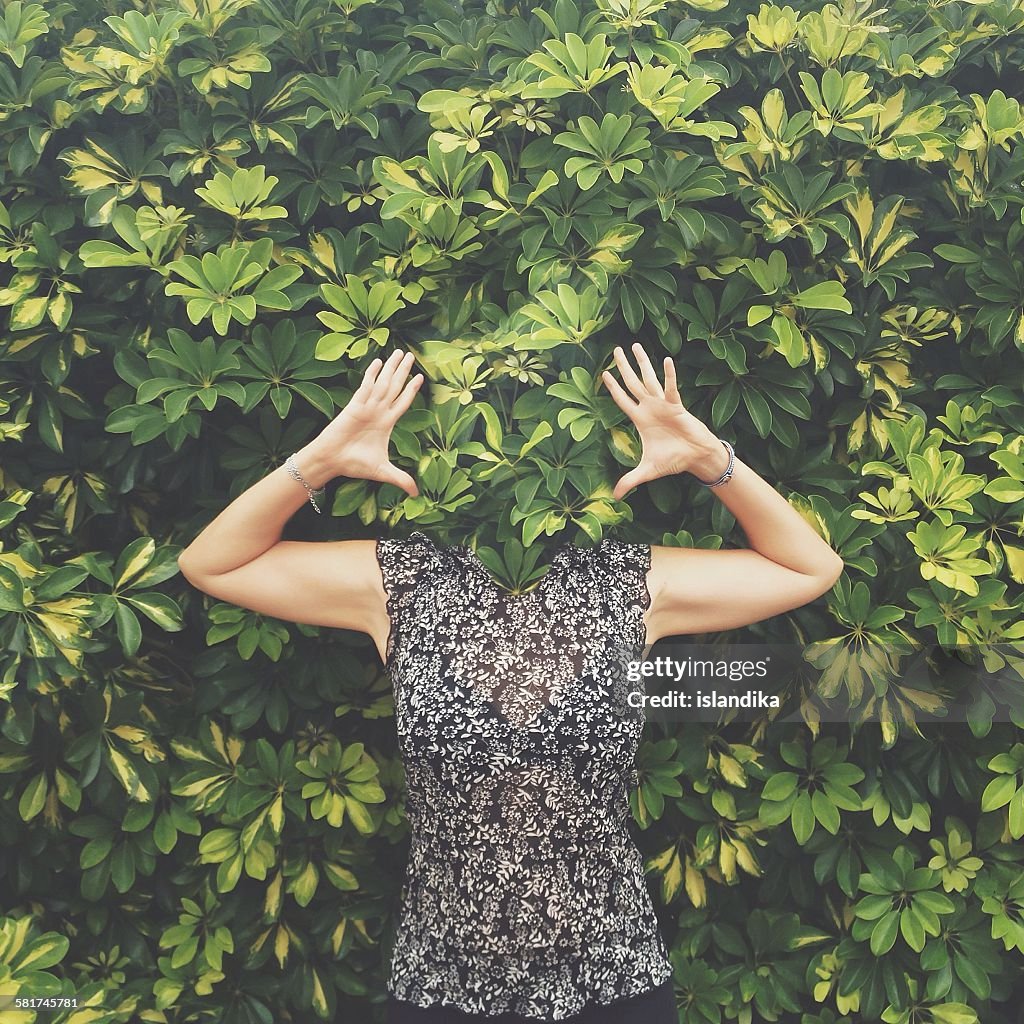 Women with face hidden behind leaves standing with raised arms