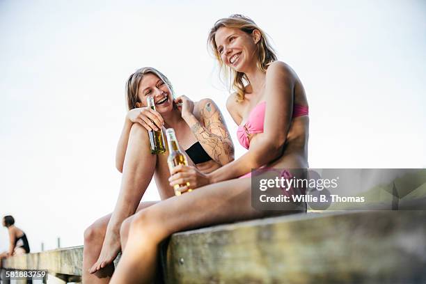 young women sitting on pier by lake - bottle water stock-fotos und bilder