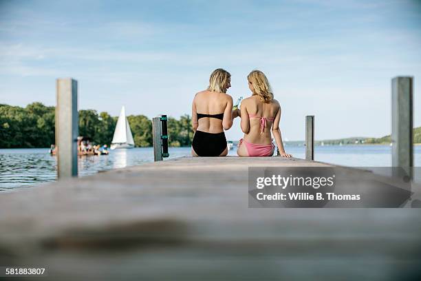 two female friends sitting on pier - steg zwei menschen stock-fotos und bilder