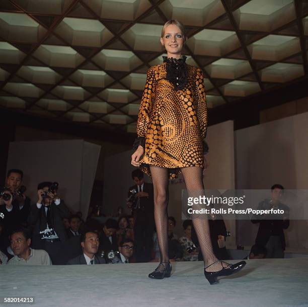 English fashion model Twiggy pictured wearing a black and orange mini dress with a lace ruff collar on a catwalk during a fashion show at the Osaka...