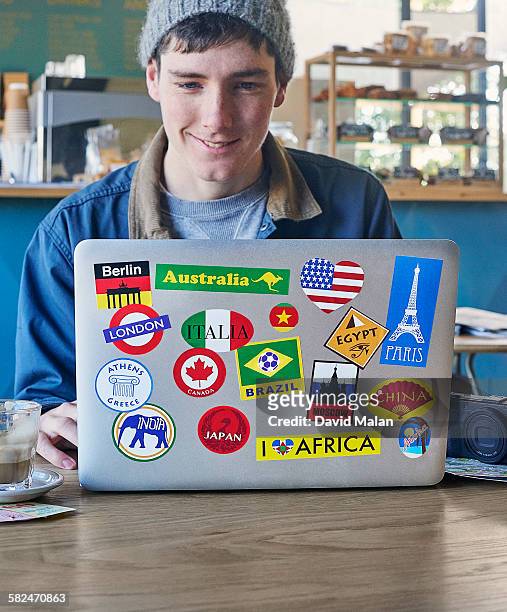 young man using a laptop with travel stickers - sticker stock-fotos und bilder
