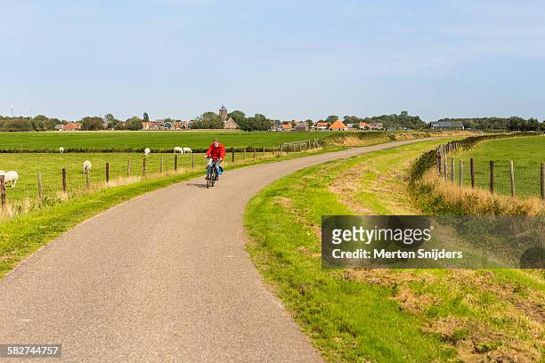 cyclist leaving village into countryside - friesland stock pictures, royalty-free photos & images