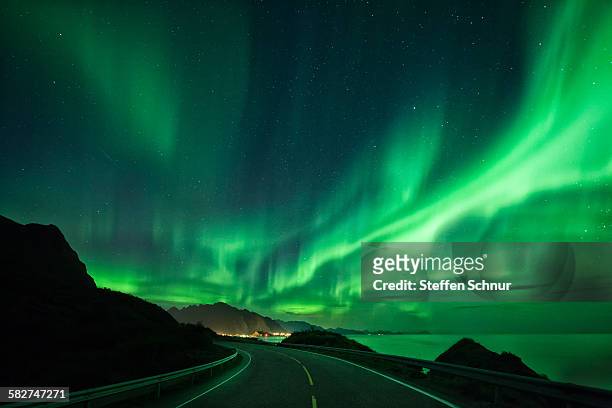 large spectacular northern lights over road & sea - noorderlicht stockfoto's en -beelden