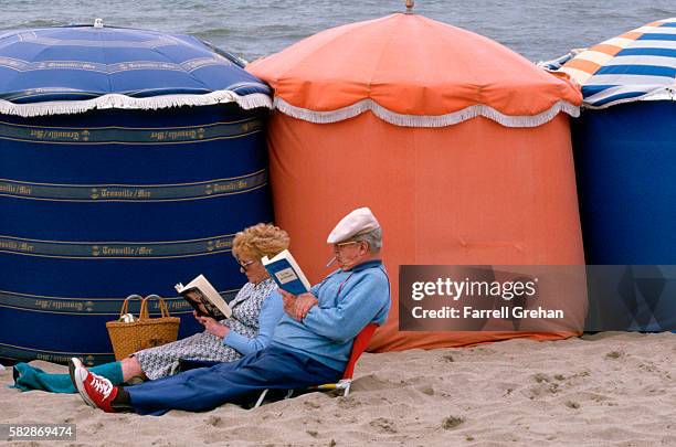 couple reading next to fabric beach tents in trouville, france - france années 60 photos et images de collection