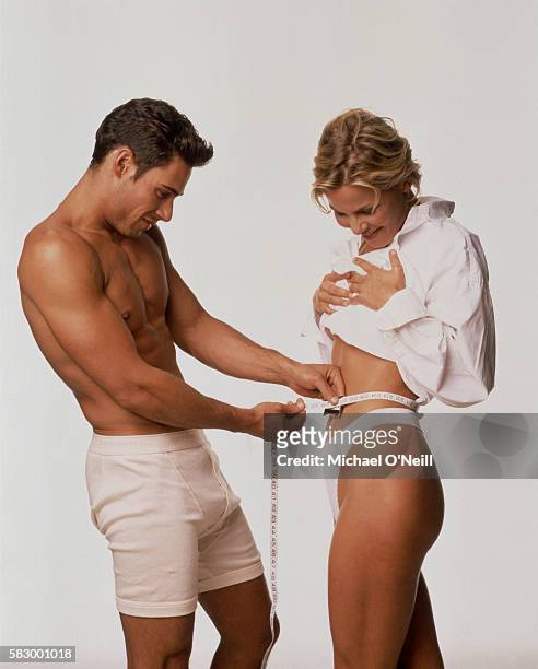 Male model wearing boxer briefs measures the waistline of a physically fit woman.