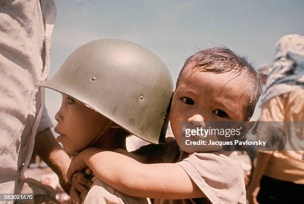 Child wearing an army helmet carries a younger infant on his back. On April 29 American forces withdrew from Saigon, leaving the noncommunist capital...