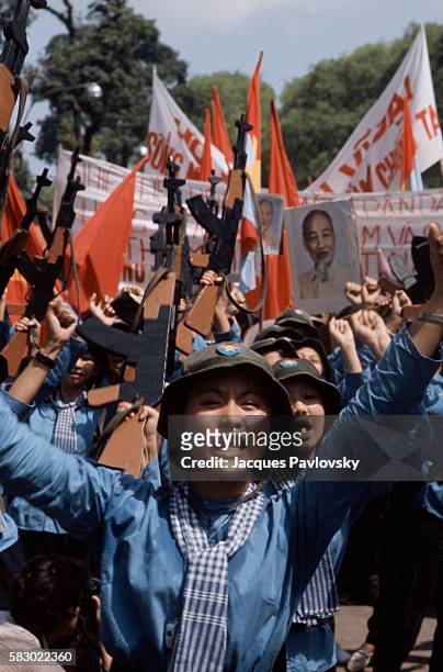 Female North Vietnamese troops enter Saigon carrying wooden rifles, red flags, and portrait of Ho Chi Minh.