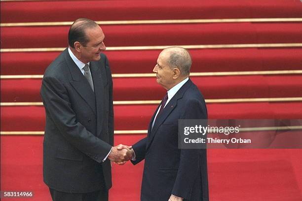 Poignée de main entre Jacques Chirac et François Mitterrand sur fond de tapis rouge.