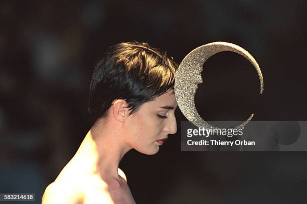 Model Erin O'Connor wearing a moon shaped hat.