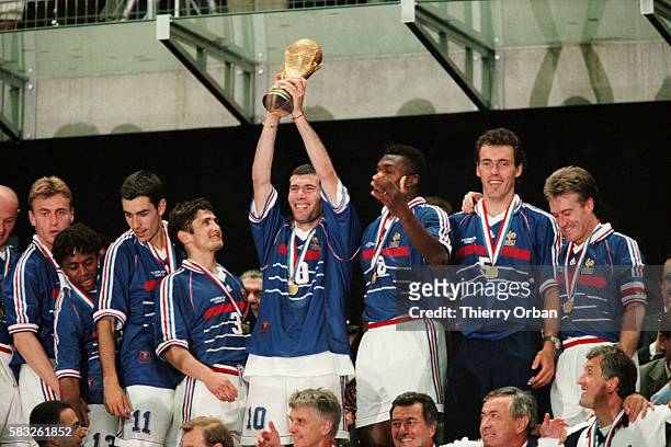 Zinedine Zidane holding the trophy with teammates after their 3-0 victory over Brazil in the final of the 1998 FIFA World Cup. | Location:...
