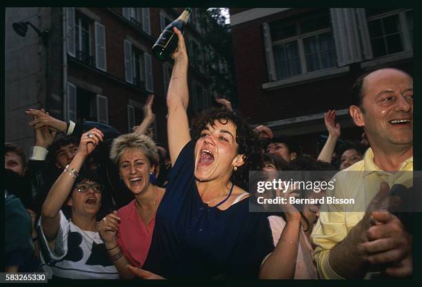 Group of people celebrate Francois Mitterrand's victory in the 1988 French presidential elections by yelling, raising their hands and opening a...