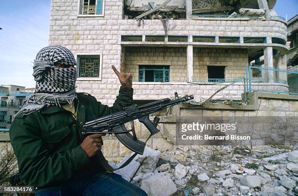 Guerrilla with the Popular Front for the Liberation of Palestine stands beside a ruined building in Beirut, wearing a kaffiyeh over his head, holding...