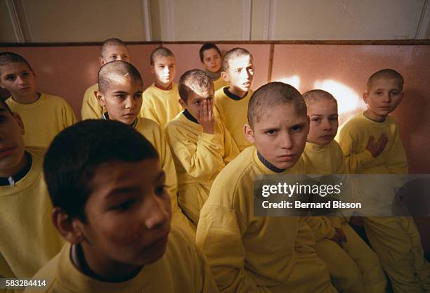 Children with shaved heads and yellow uniforms sit in rows in a classroom of a orphanage for juvenile delinquents in Bucharest, Romania.