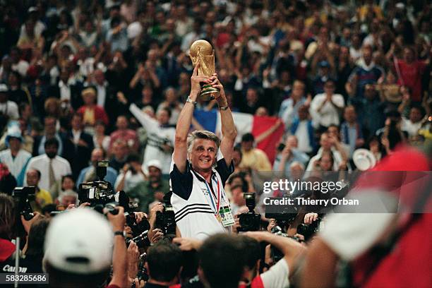 Aime Jacquet, coach of the French national team, holds up the 1998 FIFA World Cup trophy as his team carries him on their shoulders after their...