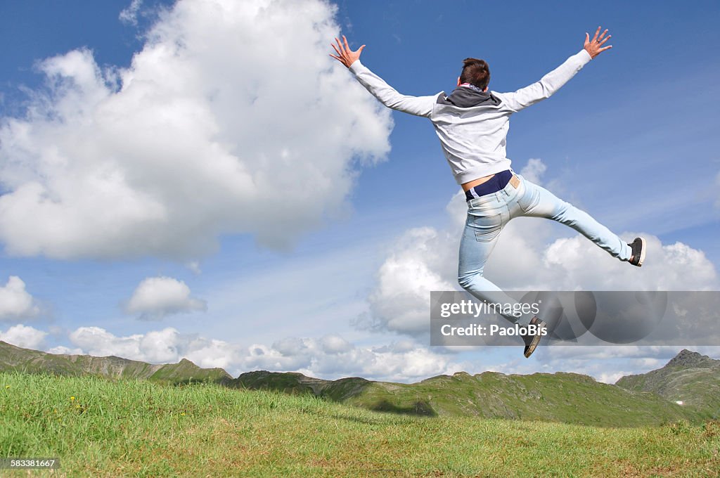 A boy is jumping with mountains in the background