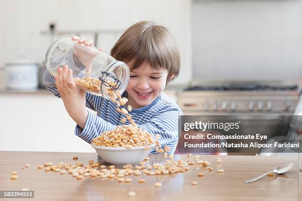 boy pouring cereal into bowl in kitchen - cereals fotografías e imágenes de stock