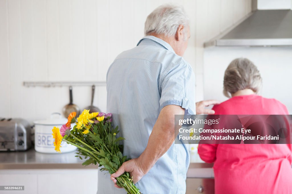 Senior man holding flowers behind back for wife
